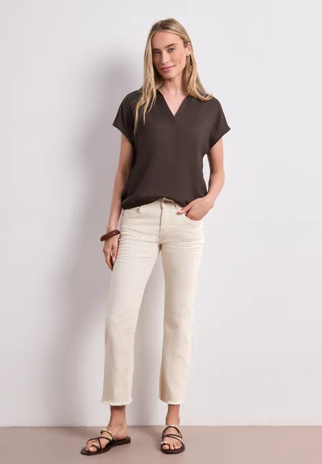 Chemisier à col chemise et ourlet élastiqué espresso brown Une femme devant un fond blanc porte un T-shirt marron, un jean clair et des sandales noires.
