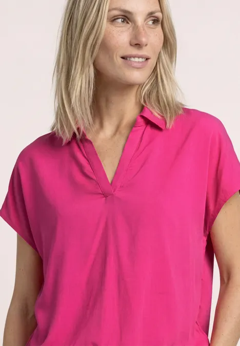 Vrouw met blond haar draagt een los vallende fuchsia top met V-hals.
