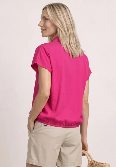Vrouw van achteren in roze shirt en beige korte broek voor lichte achtergrond.