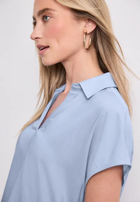 Frau in hellblauer Bluse mit V-Ausschnitt und goldenen Creolen-Ohrringen, Gesicht unkenntlich.