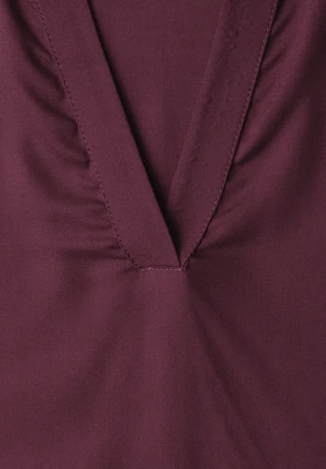 Close-up van een wijnrood kledingstuk met een diep V-hals en zichtbare stiksels