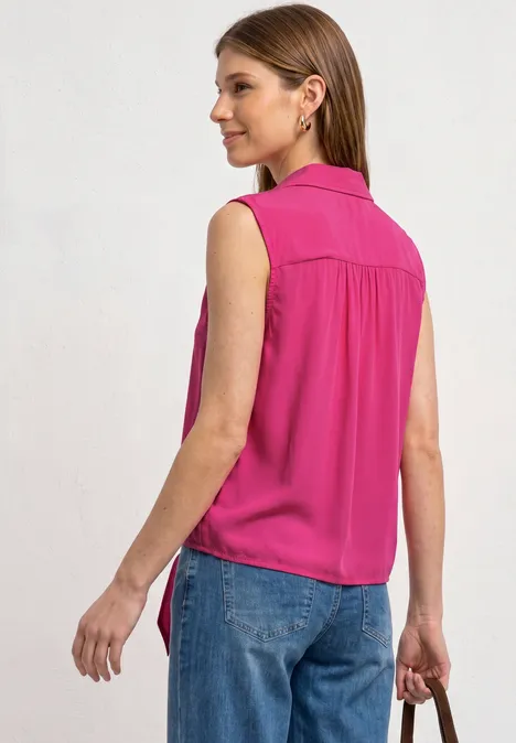 Frau von hinten in pinker ärmelloser Bluse und blauen Jeans, in der Hand eine kleine Clutch.