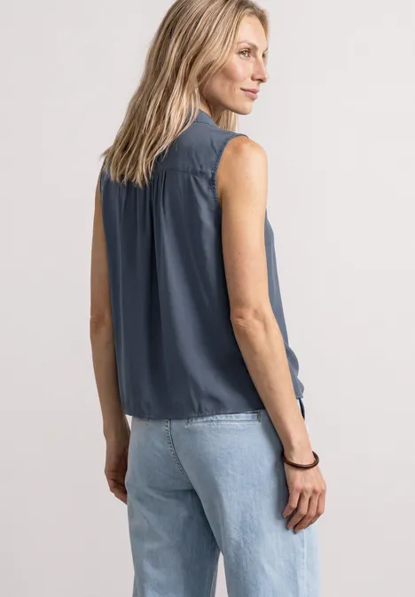 Frau in ärmelloser dunkelblauer Bluse und hellen Jeans von hinten fotografiert.