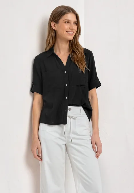 Chemisier à manches courtes à revers Black Une personne porte une chemise noire à manches courtes et un pantalon blanc sur fond blanc.