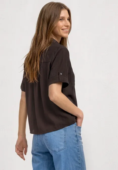 Frau von hinten in lockerem schwarzen T-Shirt und hellblauen Jeans, vor schlichtem weißem Hintergrund.