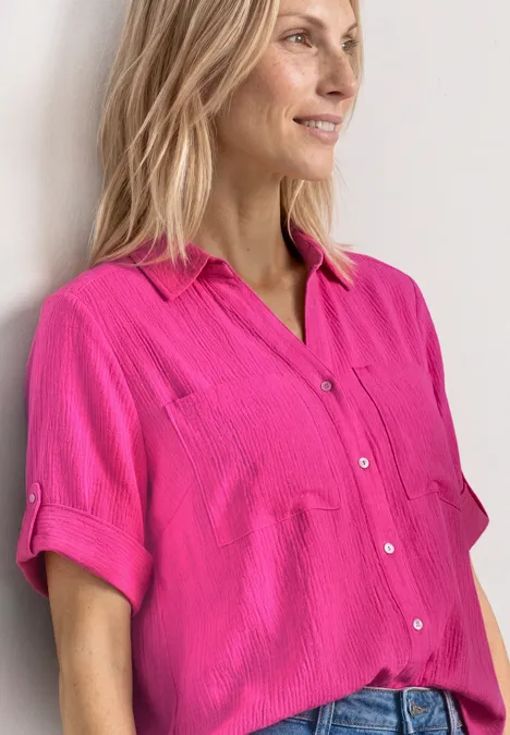 Chemisier à manches courtes à revers magenta dream Personne blonde en chemise rose manches courtes appuyée contre un mur blanc.