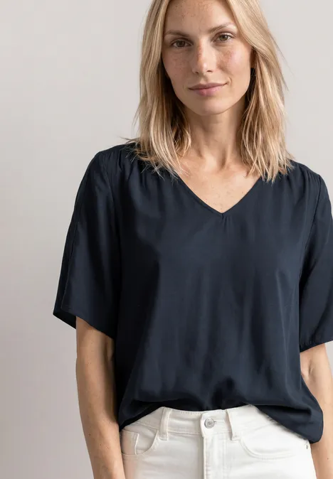 Frau in schwarzem V-Ausschnitt-Shirt und weißen Hosen, Oberkörper abgebildet.