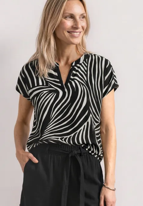Blouse met split in de hals en luipaardprint Black Een vrouw draagt een zwart-wit zebra-top en zwarte broek voor een witte achtergrond.