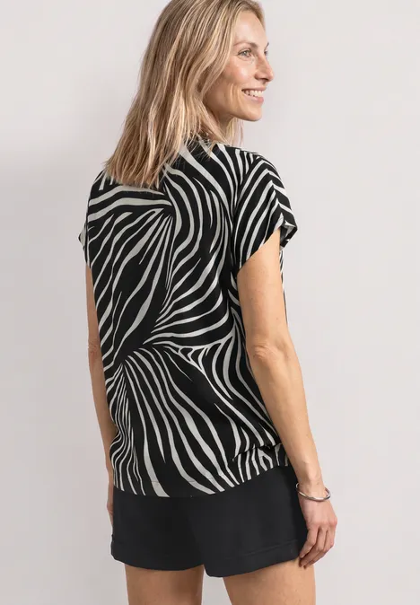 Blouse met split in de hals en luipaardprint Black Vrouw van achteren in een zwarte short en een zwart-wit zebrapatroon top, lichte achtergrond.