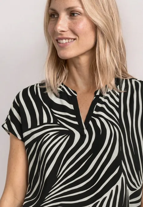 Blouse met split in de hals en luipaardprint Black Een glimlachende vrouw met blond haar draagt een kort mouw blouse in zwart-witte zebraprint.