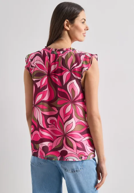 Rückansicht einer Frau in jeansblauer Hose und pinker, floraler Bluse.