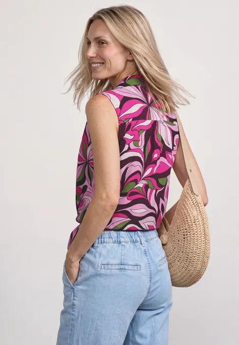 Frau von hinten mit pinkem, gemustertem Top, hellblauen Jeans und einer Strohtasche.