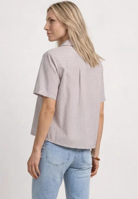 Frau in hell gestreiftem Kurzarmhemd und blauer Jeans, von hinten vor neutralem Hintergrund.