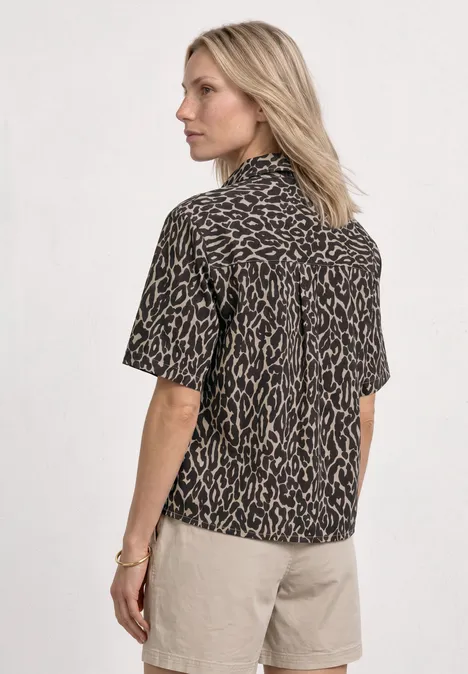 Vrouw van achteren in een korte blouse met luipaardprint en beige korte broek.