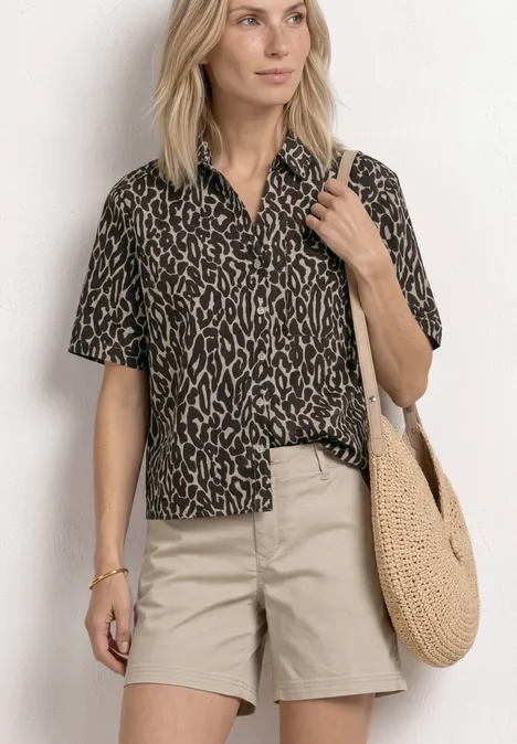 Persoon draagt kort mouw luipaardprint overhemd, beige korte broek en ronde stro tas.
