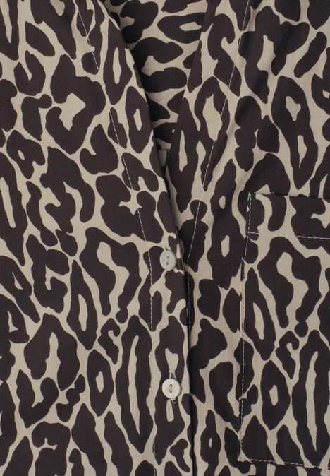 Close-up van een beige blouse met zwart luipaardprint en witte knopen.