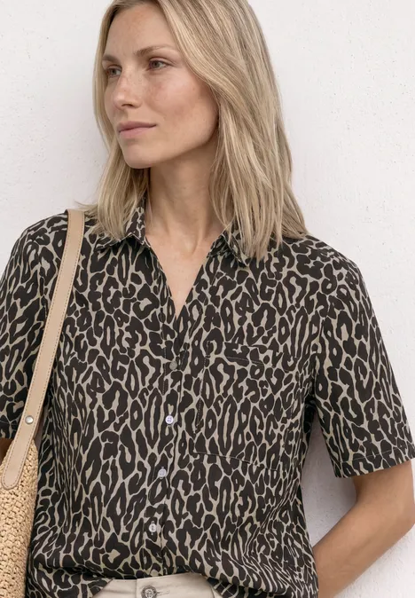 Persoon draagt een blouse met korte mouwen in luipaardprint en een strooien tas.