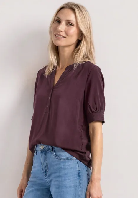 Eine Frau in einer dunkelvioletten Bluse mit hochgekrempelten Ärmeln und blauen Jeans.