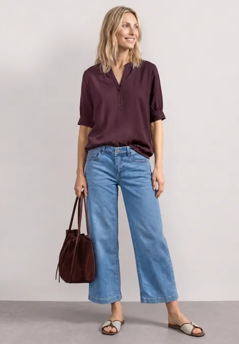 Frau trägt weite blaue Jeans, dunkelviolette Bluse, schwarze Sandalen und eine burgunderrote Tasche.