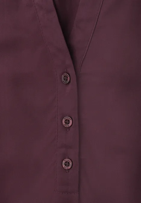 Dunkelrote Bluse mit V-Ausschnitt und drei Knöpfen.