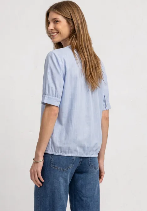 Une femme en chemise bleu clair et jean, de profil, souriante.