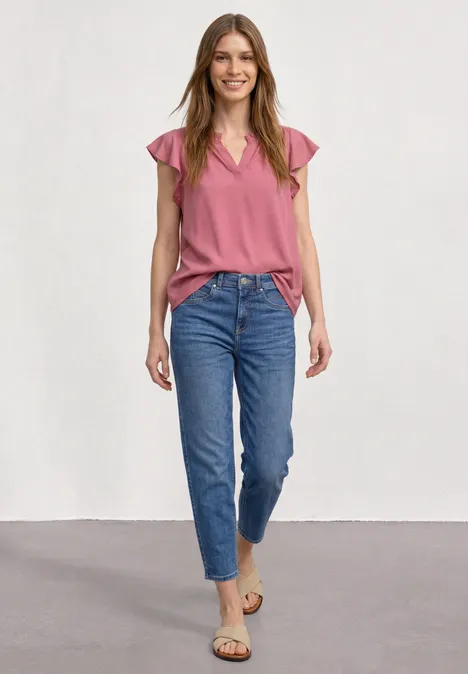 Junge Frau in Jeans und rosa Top, steht lächelnd in Studio.