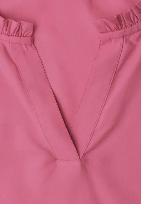 Nahaufnahme eines rosa Oberteils mit V-förmigem Ausschnitt und Rüschen an den Schultern.