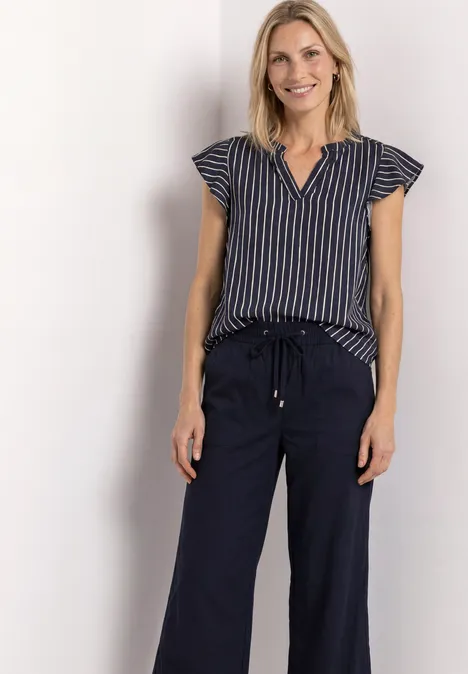 Une femme souriante portant un top rayé et un pantalon bleu marine ample à cordon, posant devant un fond clair.
