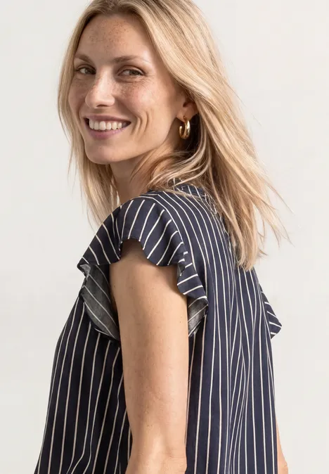 Femme blonde souriante portant un haut rayé bleu et blanc.