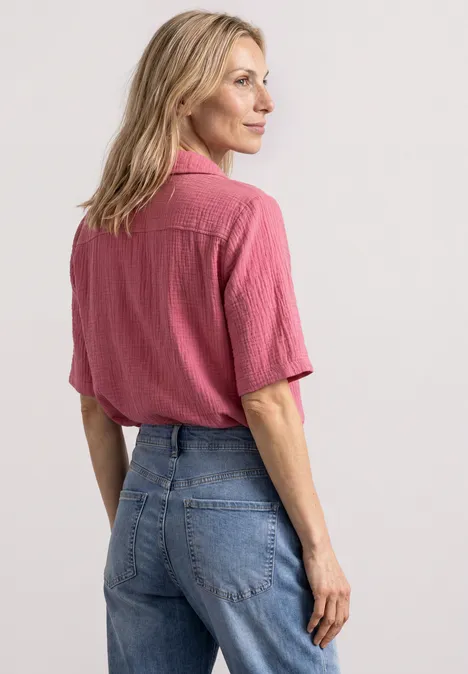 Mousselineblouse met bowlingkraag blush berry Frau von hinten in pinker Bluse mit kurzen Ärmeln und blauer Jeans.