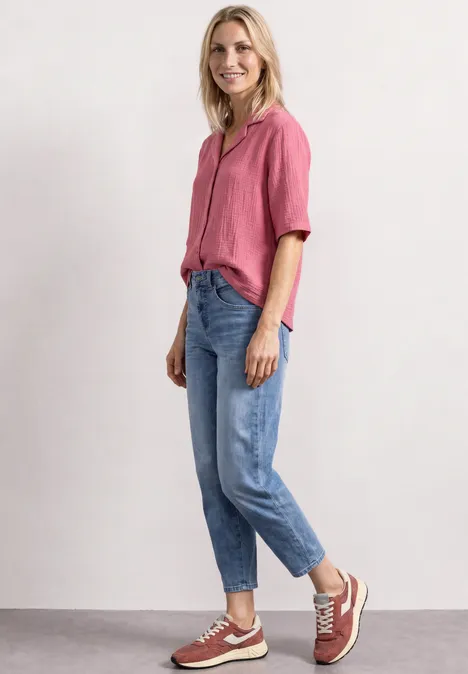 Mousselineblouse met bowlingkraag blush berry Eine Frau in rosa Bluse und Jeans steht und lächelt