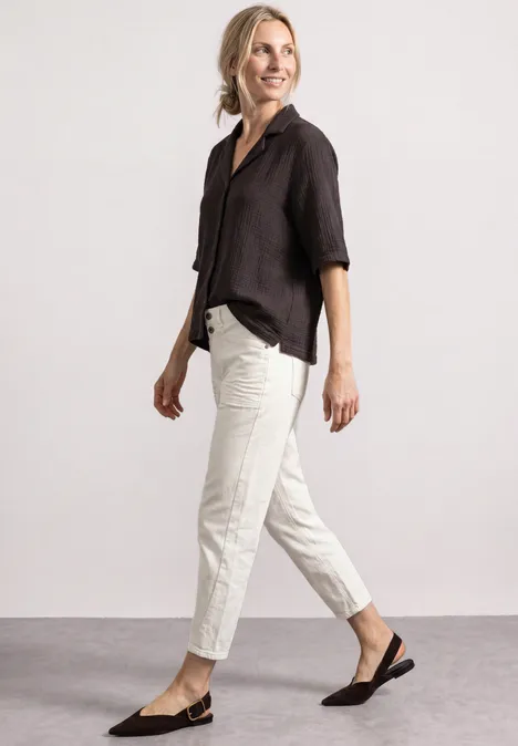 Mousselineblouse met bowlingkraag black coffee Frau in schwarzer Bluse, hellen Hose und schwarzen Slingback-Pumps vor neutralem Hintergrund.