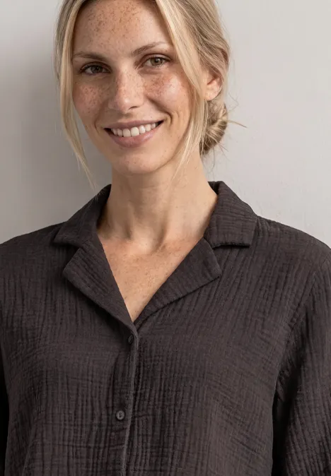 Mousselineblouse met bowlingkraag black coffee Eine lächelnde blonde Frau in einem dunkelgrauen Hemd vor neutralem Hintergrund.