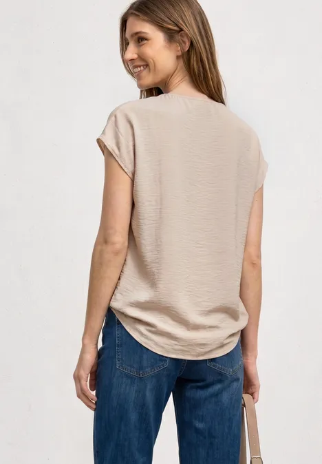 Eine Frau steht von hinten in beigem T-Shirt, blauen Jeans und hält eine Tasche.