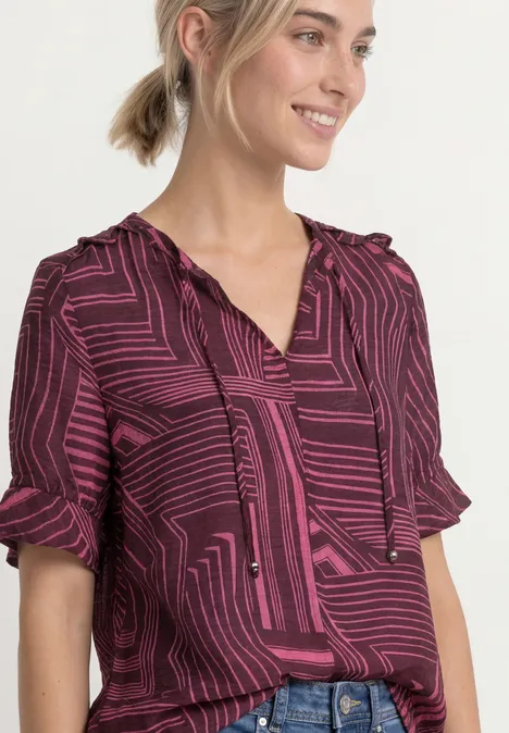 Frau trägt eine violett-pinke Bluse mit geometrischem Muster und kurzen Ärmeln.