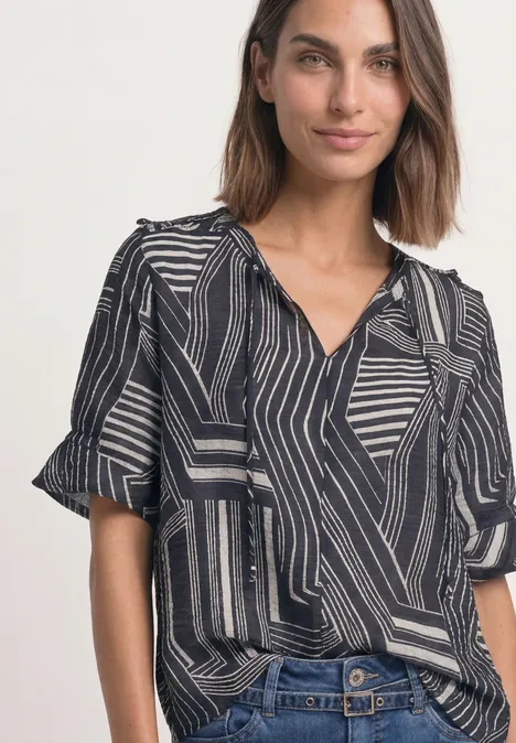 Frau trägt gemusterte schwarz-weiße Bluse mit geometrischem Design und Jeans.