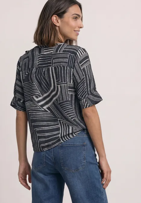 Frau von hinten in Jeans und kurzärmeligem Oberteil mit geometrischem Muster.