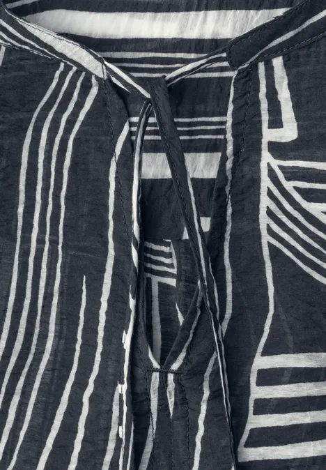 Nahaufnahme eines dunkelblauen Shirts mit weißem, geometrischem Streifenmuster und Bändchen am Ausschnitt.