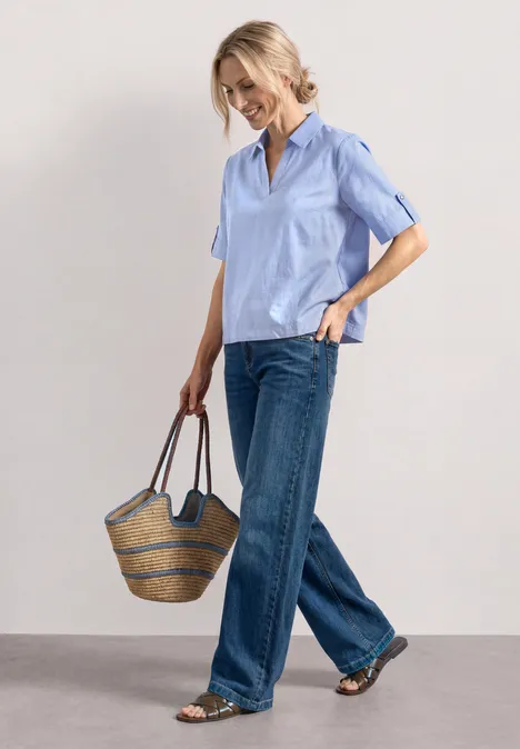 Chemisier à manches courtes en chambray avec col chemise original blue Femme en chemise bleu clair à manches courtes, jean ample et sac en paille, marche avec décontraction.