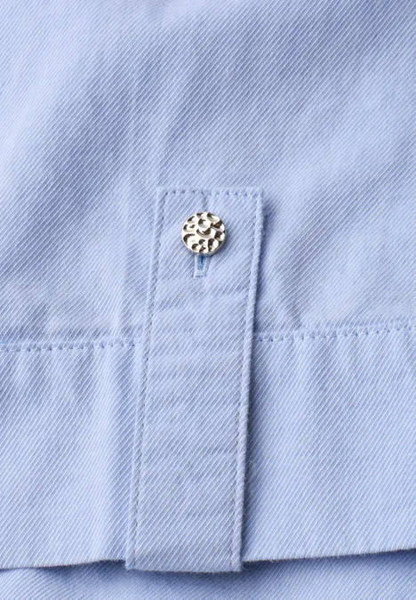 Chemisier à manches courtes en chambray avec col chemise original blue Gros plan d'un bas de chemise bleu clair avec un bouton-pression métallique décoratif.