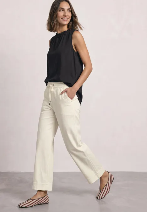 Blouse met gerimpelde ronde hals Black Frau in schwarzer ärmelloser Bluse, hellen weiten Hosen und gestreiften Sandalen, die selbstbewusst geht.