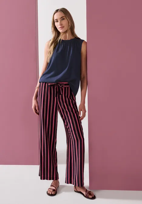 Blouse met gerimpelde ronde hals darkest blue Eine schlanke Frau trägt ein ärmelloses dunkles Oberteil und weit geschnittene Streifenhose vor rosa-weißem Hintergrund.