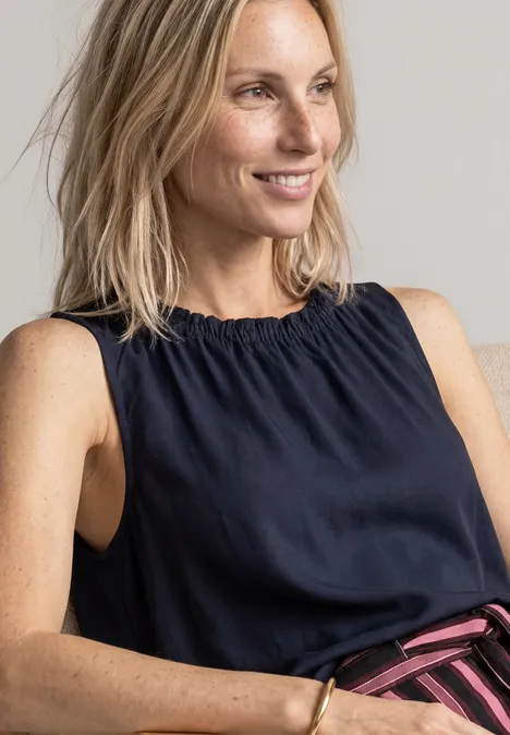 Blouse met gerimpelde ronde hals darkest blue Lächelnde blonde Frau in ärmellosem dunkelblauen Top vor neutralem Hintergrund.