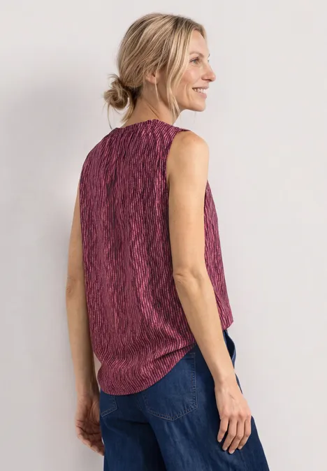 Femme vue de dos, coiffure en chignon, débardeur rose à motif ondulé et jean bleu.