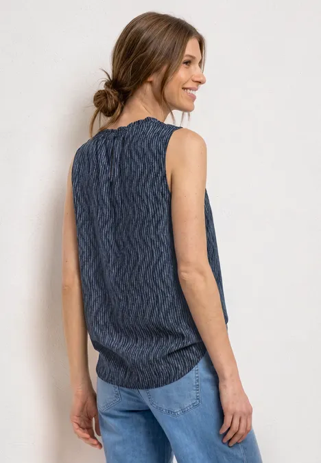 Femme de dos portant un top sans manches bleu marine à motif ondulé et un jean clair, cheveux noués en chignon.