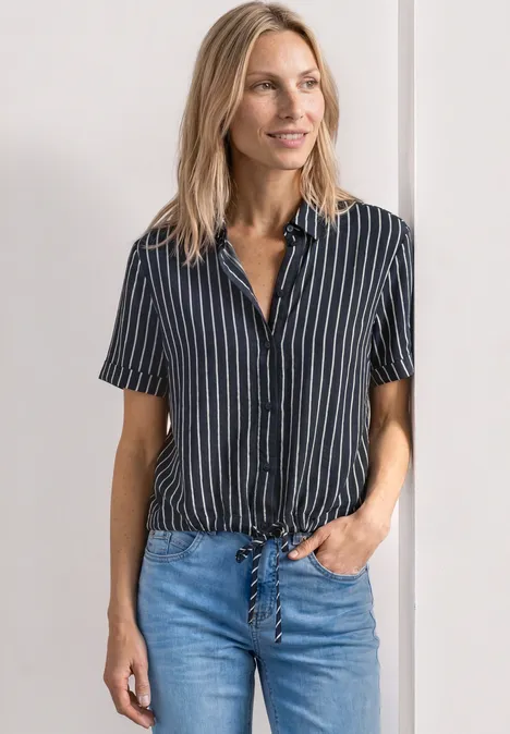 Une femme porte une blouse à manches courtes rayée bleu-blanc nouée à la taille et un jean bleu.