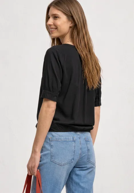 Frau von hinten in schwarzer Bluse, blauen Jeans und mit einer roten Tasche.