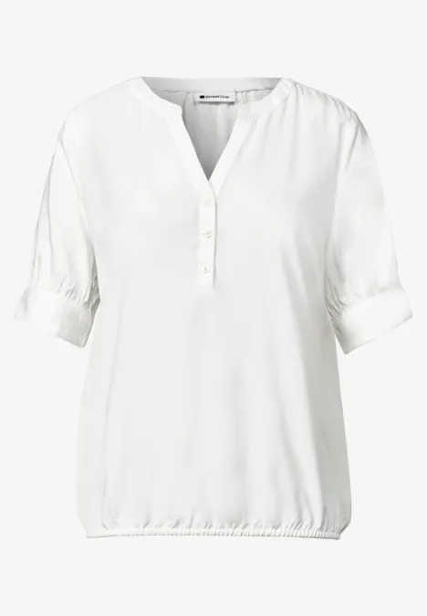 Blouse blanche col en V avec patte de boutonnage courte et ourlet élastiqué.