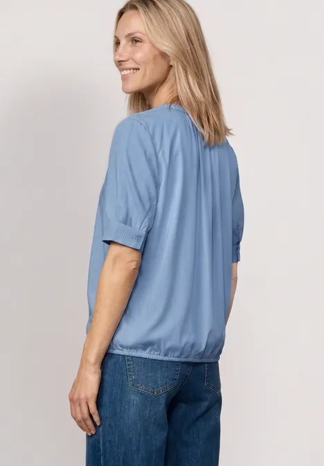 Blouse met korte mouwen, split in de hals en elastische zoom northern blue Vrouw van achteren, draagt lichtblauw shirt en spijkerbroek.