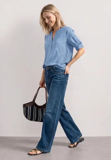 Blouse met korte mouwen, split in de hals en elastische zoom northern blue Vrouw in lichtblauw overhemd, wijde jeans, sandalen en gestreepte handtas op neutrale achtergrond.